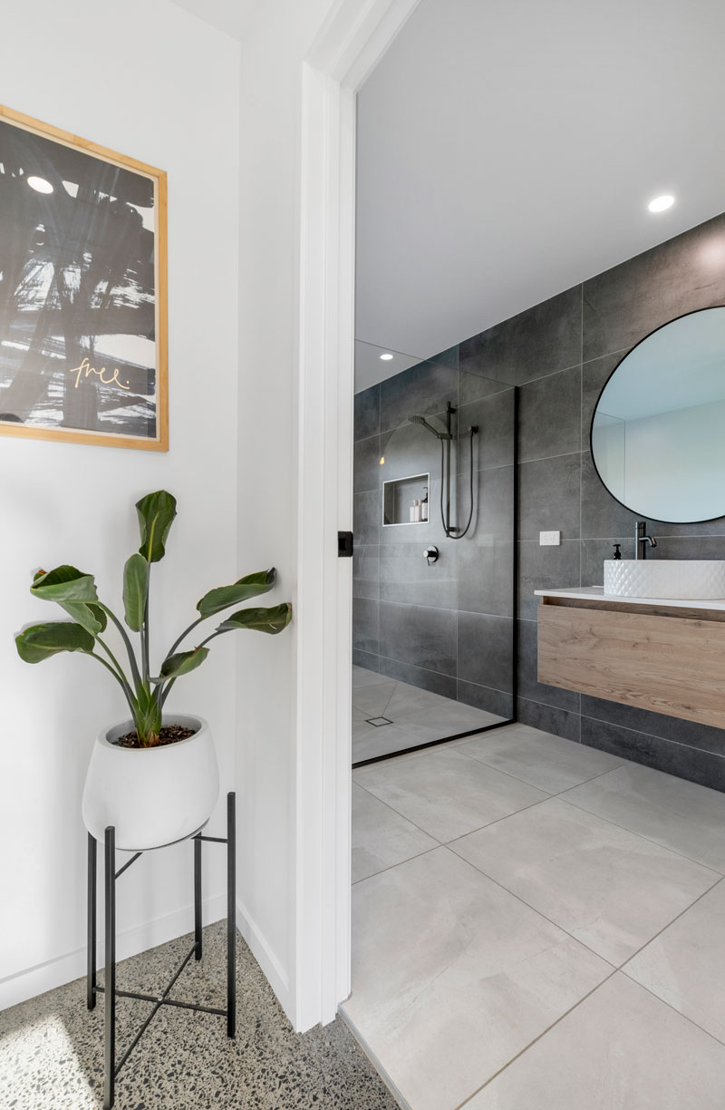 Gorgeous ensuite bathroom with large round mirror, charcoal tile feature wall and timber New Tech vanity