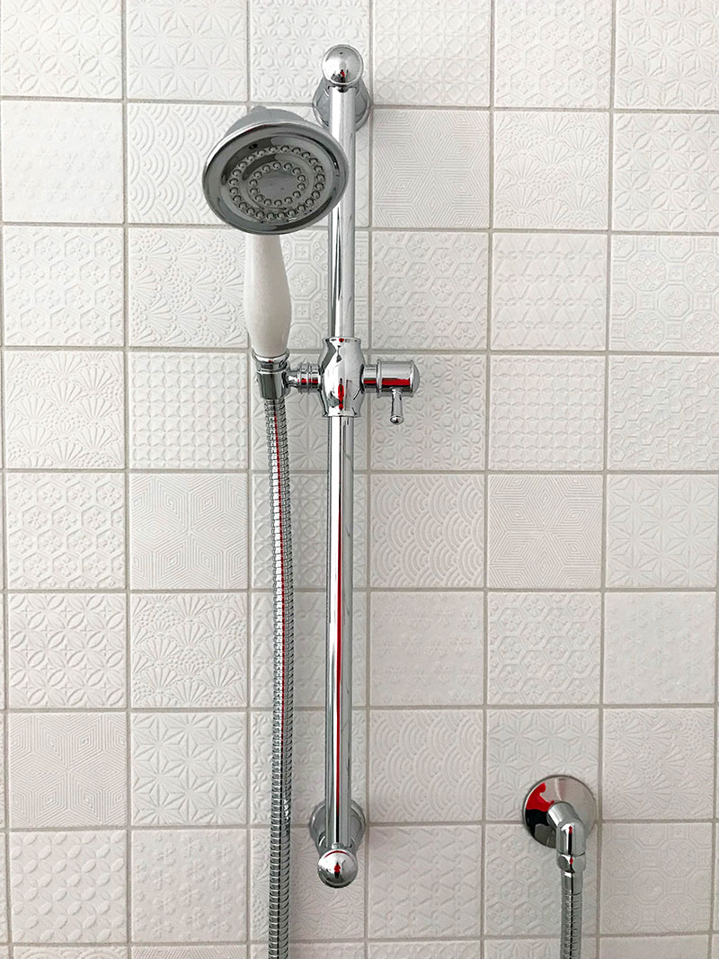 Close up of gorgeous traditional style shower head on stunning white patchwork style, mosaic tiles 