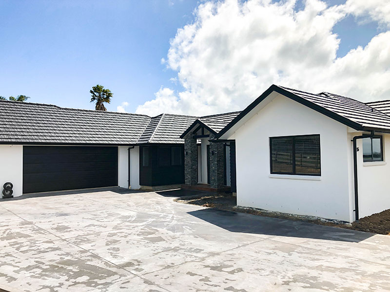 Entrance to new home with schist pillars, black front and garage door, white plaster and black weatherboards