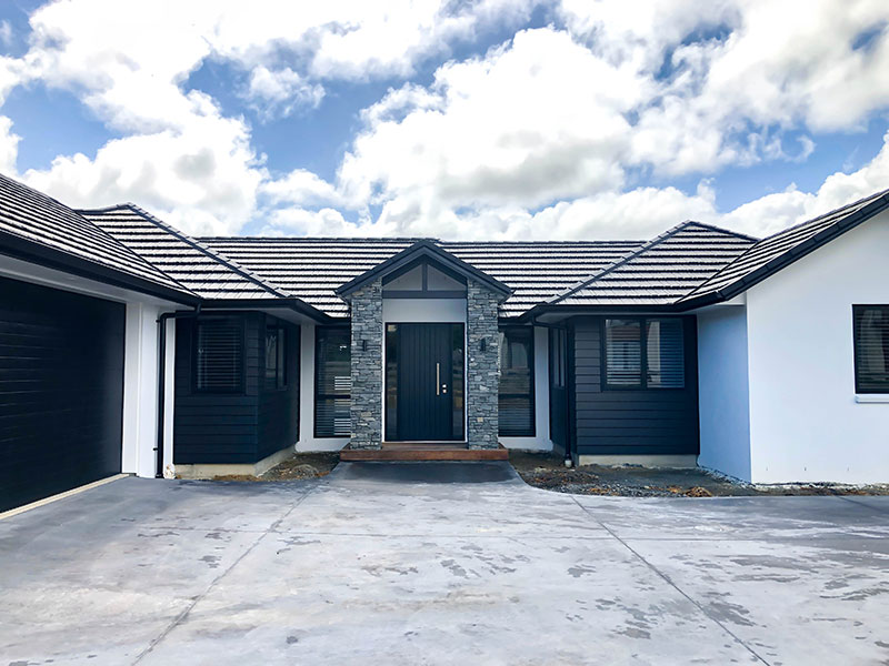 Black weatherboards, white plaster and schist pillars with black garage door and front door on front of this home