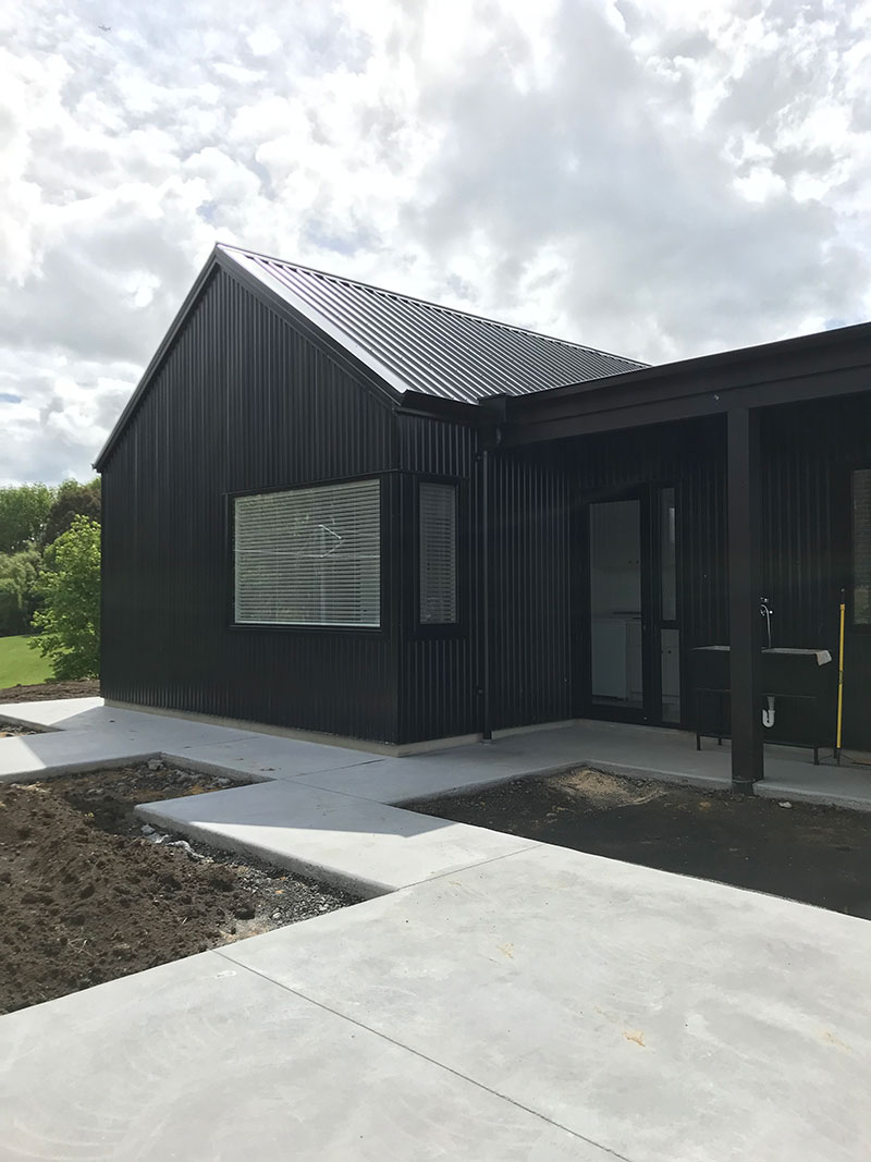 Exterior of black barn style house with path leading to laundry and back door