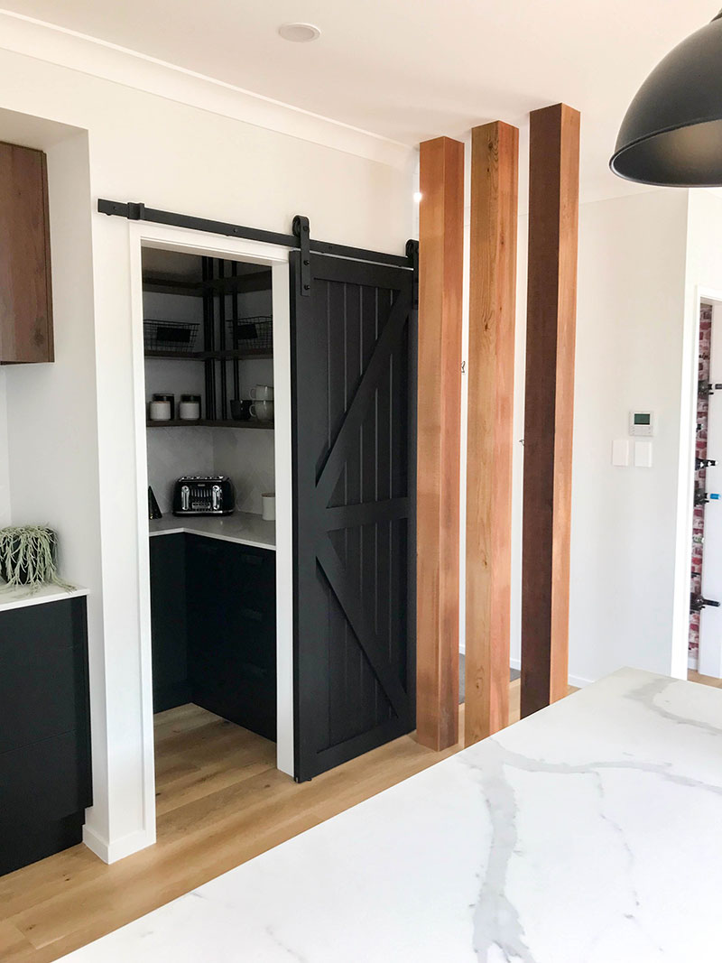 Striking Black barn door as entrance into scullery and beatiful cedar lined posts in showhome kitchen at Paerata Rise