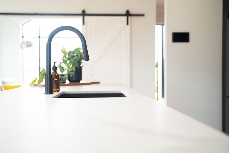 Gorgeous white marble bench with black tap & sink & pot plant. Large white barn doors in background leading to vaulted lounge