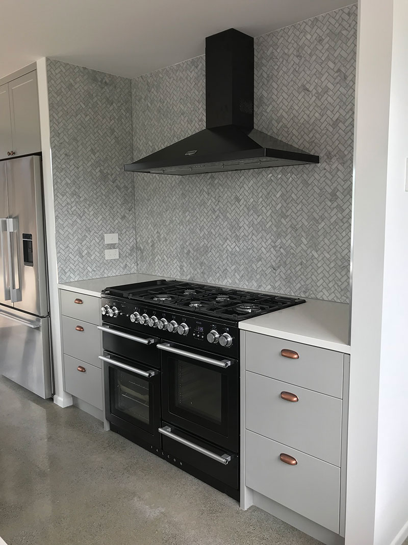 Stunning, marble, herringbone mosaic tiled splashback with large black falcon oven & stove & black rangehood