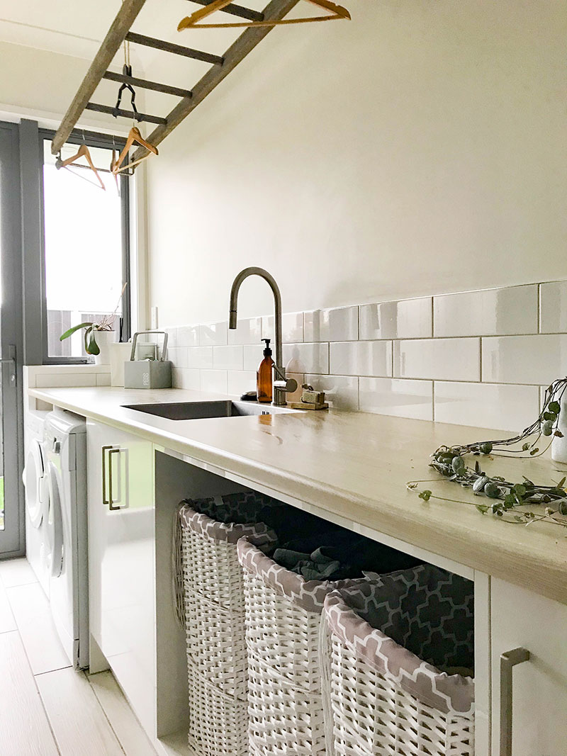 Beautiful, light laundry room with rustic suspended ladder for drying and white cane baskets