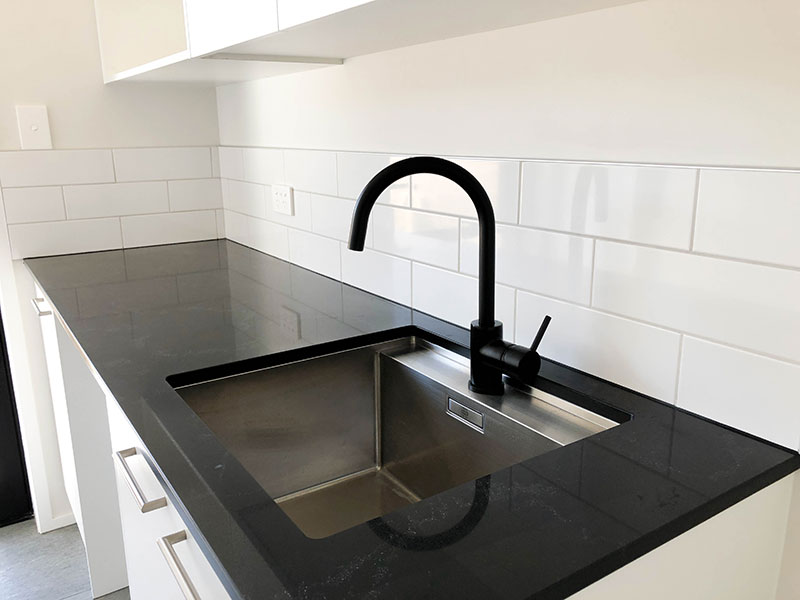 Stunning black and white laundry with black benchtop, black tap and white subway splashback